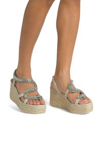 Sandales compensées beiges avec une semelle en jute tressé, présentant un design de serpent métallique décoratif orné de strass sur la bride.