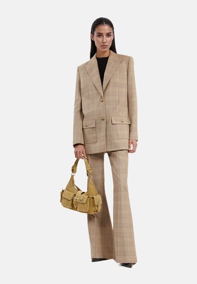 Blazer de cuadros beige y pantalones acampanados a juego, con dos bolsillos frontales y botones dorados. Sosteniendo un bolso de ante mostaza con múltiples compartimentos.