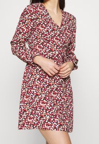 Abito con stampa floreale, caratterizzato da maniche lunghe, scollo a V e vita aderente. Il motivo vivace include fiori rossi, rosa e blu su uno sfondo scuro.