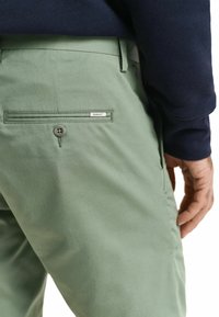 Grønne bomullsbukser med en glatt tekstur, med en baklomme, knappelukking, og en GANT-etikett på lommen.