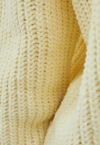 Teksturowana, bladożółta tkanina prezentująca dziergany wzór z wypukłymi ściegami, miękką puszystą fakturą i subtelnym połyskiem.