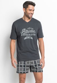 T-shirt gris foncé à col en V avec un imprimé graphique ; associé à un short à carreaux noir et gris avec un motif géométrique et des coutures contrastantes.