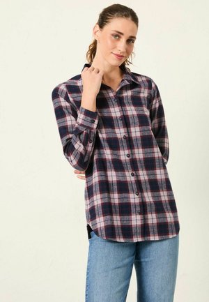 Navy and grey plaid flannel shirt with long sleeves, button front, and side slits. Paired with light blue jeans.