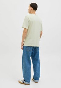 Lys grøn bomulds t-shirt med korte ærmer, parret med løstsiddende blå denim jeans og hvide sneakers, vist fra bagenden.
