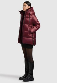 Burgundy puffer jacket with a hood, zippered pockets, and black hardware. Smooth, shiny surface with a fitted silhouette and horizontal stitching.