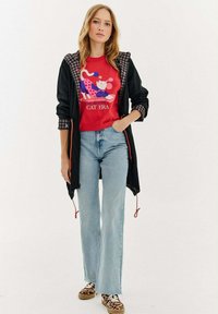 Czarna kurtka z kapturem z wzorzystą podszewką, czerwona koszulka z grafiką, jasnoniebieskie dżinsy dzwony oraz trampki w zwierzęcy wzór z teksturowaną powierzchnią.