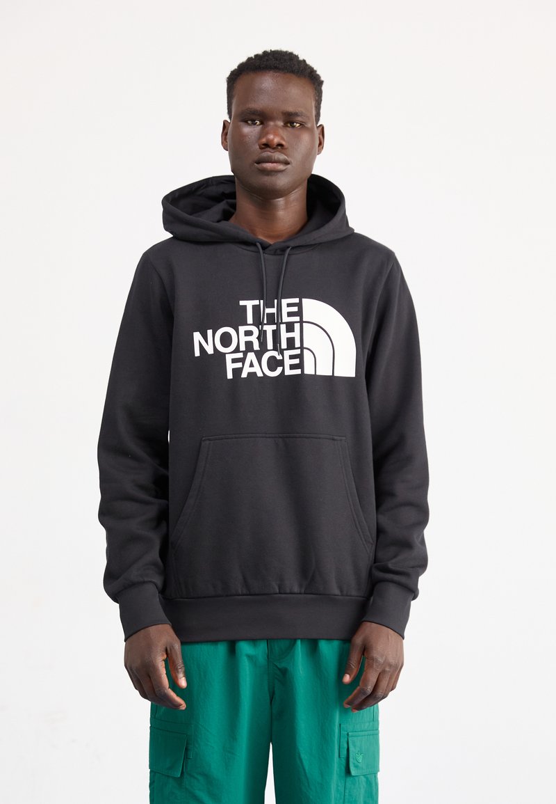 Zwarte hoodie met een buidelzak en witte logo tekst. Draag het met groene cargobroek met een relaxed fit en een zachte textuur.