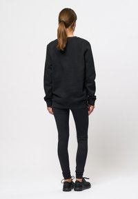 Zwarte sweatshirt met lange mouwen, ronde hals, gedragen over zwarte leggings; gladde textuur, comfortabele pasvorm en minimale ontwerpdetails.