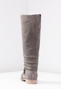 Bota de ante gris hasta la rodilla con un diseño flexible, que cuenta con un cierre de cremallera en la parte trasera y un tacón de madera plano. Acentuada con un detalle atado en el tobillo.