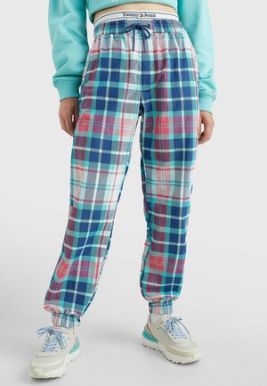 Person trägt blau-grün-pink karierte Hosen mit elastischen Bündchen, weiße Turnschuhe und ein kurz geschnittenes türkisfarbenes Sweatshirt.