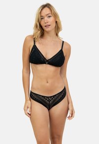 Ensemble de lingerie en dentelle noire comprenant un bralette avec des bretelles réglables et une culotte transparente avec un motif, des bords festonnés et un détail central.