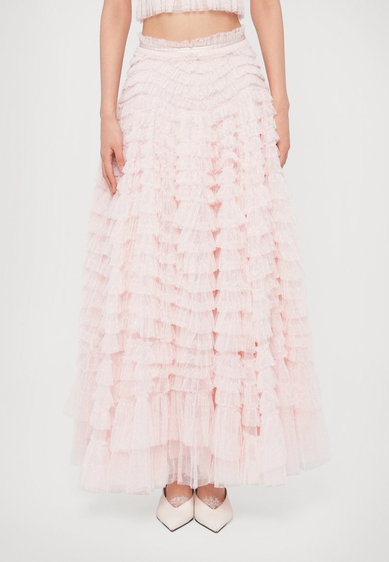 Ροζ φούστα με βολάν, φτιαγμένη από διάφανο ύφασμα με στρώσεις βολάν. Διαθέτει ελαστική μέση και ρέουσα σιλουέτα. Συνδυασμένη με λευκά παπούτσια.