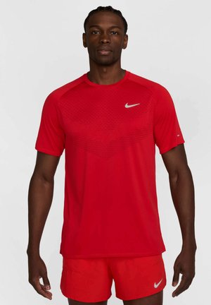 Czerwona koszulka sportowa z lekkiego materiału, z teksturowanym wzorem i srebrnym logo Nike na piersi oraz krótkimi rękawami.