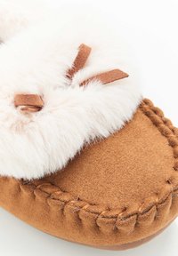 Pantofola in camoscio marrone con un morbido polsino in ecopelliccia bianca, dotata di laccetti in pelle marrone decorativi e cuciture a contrasto lungo la soletta.