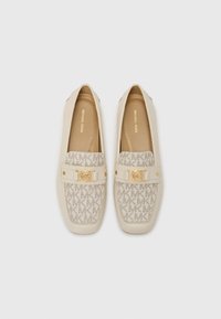 Beige loafers featuring a patterned canvas upper with "MK" logos, gold-tone hardware, and a smooth leather trim. Flat soles for comfort.