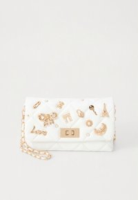 Bijela prešivena torba s zlatnim detaljima, ukrašena raznim ukrasnim privjescima uključujući mašnu, Eiffelov toranj i ključ. Uključen lančani remen.