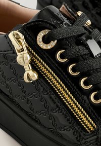 Schwarze lackierte Sneaker mit goldenen Akzenten, einem dekorativen Reißverschluss, flachen schwarzen Schnürsenkeln und einem geprägten Musterdetail im Obermaterial.