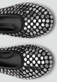 Zapatos planos de color negro mate cubiertos de tacos circulares metálicos, con punta redonda y una textura de tela suave, con un diseño de fácil colocación.