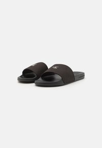 Infradito neri con tomaia in tessuto morbido e suola in gomma. Il design open-toe presenta una larga fascia curva con dettagli del logo.