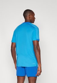 Blue athletic t-shirt with short sleeves and a crew neck. Made of lightweight material with a smooth texture. Logo detail near the hem.