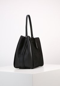 Černá kabelka z hladké kůže s vroubkovanou strukturou. Obsahuje dvě uchy, má strukturovaný trojúhelníkový tvar a decentní kovové akcenty.