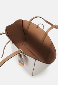 Sac cabas en cuir blanc et beige avec double bretelle et étiquette en tissu colorée attachée à une des boucles de la sangle.