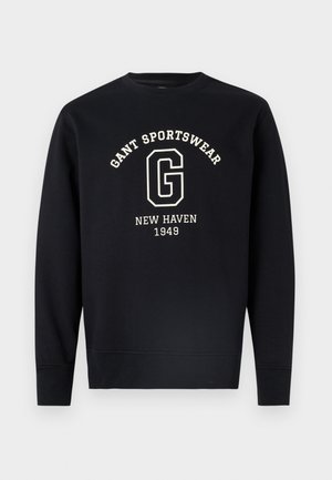 Černá mikina s dlouhým rukávem s bílým nápisem "GANT SPORTSWEAR," velkým písmenem "G" a textem "NEW HAVEN 1949" na přední straně.