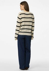 Crème gebreide trui met zwarte horizontale strepen, lange mouwen, open geweven textuur, gecombineerd met donkerblauwe wijde jeans.