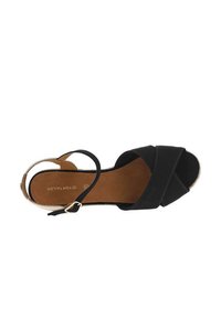 Black, cross-strap sandal with a textured upper and brown interior. Features a small buckle and a neutral outer edge. Flat sole design.