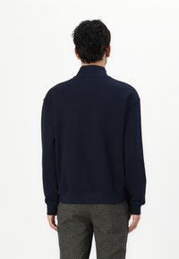 Marineblå bomulds sweater med høj krave, afslappet pasform og ribbede cuffs. Glat tekstur og minimale designdetaljer.