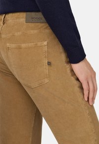 Pantaloni in corduroy color khaki con una texture a righe verticali, dotati di una tasca posteriore e una patch in pelle con logo in vita.
