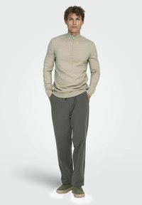 Bežinė zip-up megztinis su lankstytomis rankovėmis, derinama su laisvomis pilkomis tekstūruotomis kelnėmis ir žaliomis slip-on bateliais. Minimalistinis dizainas, neutralios spalvų paletė.