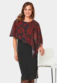 Robe noire avec une cape translucide à motif floral rouge. La cape présente un bord festonné et un subtil éclat, rehaussant l'ensemble du design.