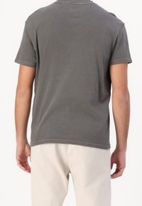 Šedé tričko s krátkým rukávem a volným střihem, s jemným logem na zadní straně, měkký bavlněný materiál a kulatý výstřih.