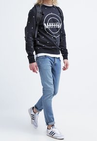 Felpa nera con stampa grafica bianca e piccoli motivi a triangolo, abbinata a jeans azzurri chiari e scarpe da ginnastica grigie con strisce.