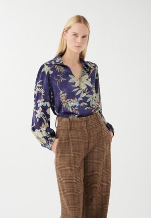 Bluse mit floralem Muster in Lila, V-Ausschnitt und langen Ärmeln, kombiniert mit braunen karierter High-Waist-Hose mit Seitentaschen.