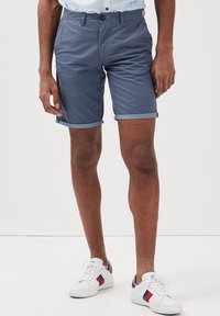 Mörkblå shorts med en strukturerad mönster, rullade muddar och sidofickor. Kombinerat med vita sneakers med röda och mörkblå detaljer.