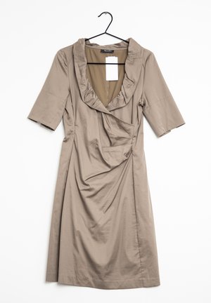 Vestido beige con escote con volantes, mangas cortas y cintura fruncida, con textura suave y diseño minimalista. Cuelga de un gancho negro.