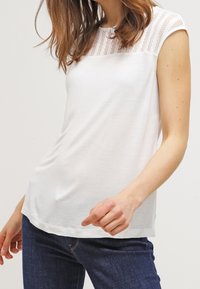 Vit kortärmad topp med en texturerad stickad panel på axlarna, med en avslappnad passform och mjukt tyg. Bar med mörka jeans.