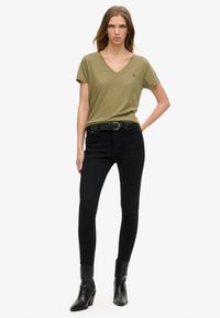 Olivengrøn V-udskærings T-shirt lavet af blødt stof, parret med sorte tætsiddende jeans og sorte ankelstøvletter med en lille hæl.