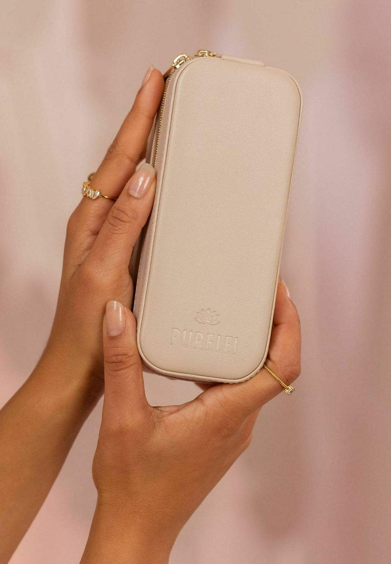 Beige, rechteckiges Etui mit glatter Textur, goldenem Reißverschluss, geprägtem "PURELEI"-Logo und abgerundeten Kanten, von einer Hand gehalten.
