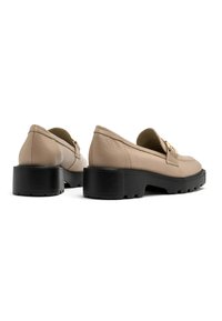 Beige leren loafers met een zwarte rubberen zool, met een gestructureerde afwerking en gouden hardwareaccenten. Chunky hak verhoogt de stabiliteit.
