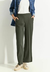 Mørkegrønne bukser med bred benvidde i struktureret stof, der har en flad talje og sidelommer, sammen med en hvid top og en denimjakke.