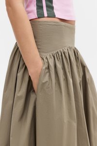 Gonna khaki con texture arricciata e vita elastica, dotata di tasche laterali. Il top è corto, in tessuto rosa con strisce verdi.