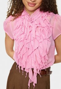 Rozā blūze ar augstu rīkļveida apkakli, īsām piedurknēm un slāņotu dizainu ar izplūdušiem malām, papildināta ar brūnu jostu.