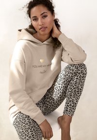 Sudadera beige con estampado dorado, combinada con leggings ajustados de leopardo. Tejido suave, corte relajado y textura visible en la ropa.
