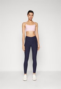 Lys rosa trenings-bh med tynne stropper kombinert med mørkeblå tettsittende leggings. Begge plaggene har en glatt tekstur og et minimalistisk design.