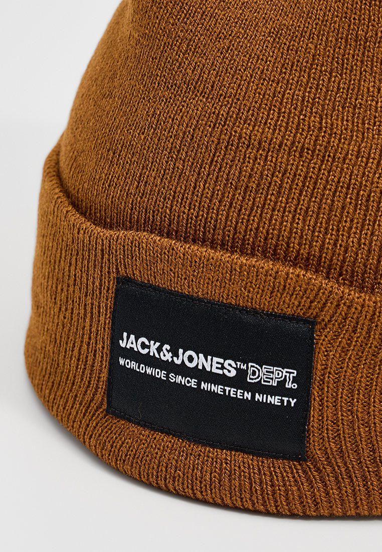 Bruine gebreide beanie met een ribbelstructuur. Bevat een zwart label met het "JACK & JONES"-logo en de slogan "WERELDWIJD SINDS NEGENTIEN NEGENTIG."
