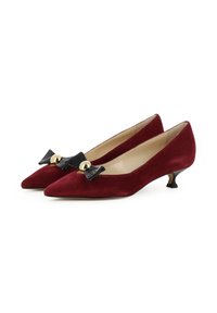 Décolleté in suede rosso con punta affusolata e un piccolo fiocco nero decorato con un accento dorato sulla parte anteriore. Presenta un tacco kitten.