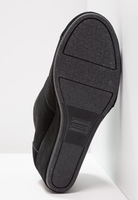 Scarpa in suede nero con suola in gomma testurizzata. La suola presenta una forma arrotondata con il logo TOMS e linee di presa orizzontali.